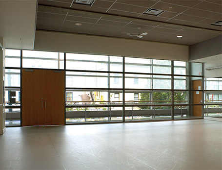 An empty dance studio with mirrors and windows with the blinds half closed.