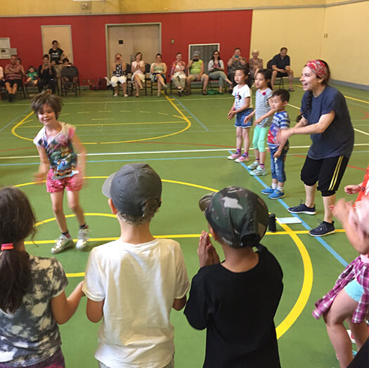 Elementary school students taking part in a dance class in a gym.