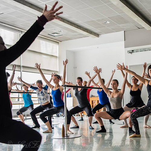 Dance students bend with arms raised in an open house class