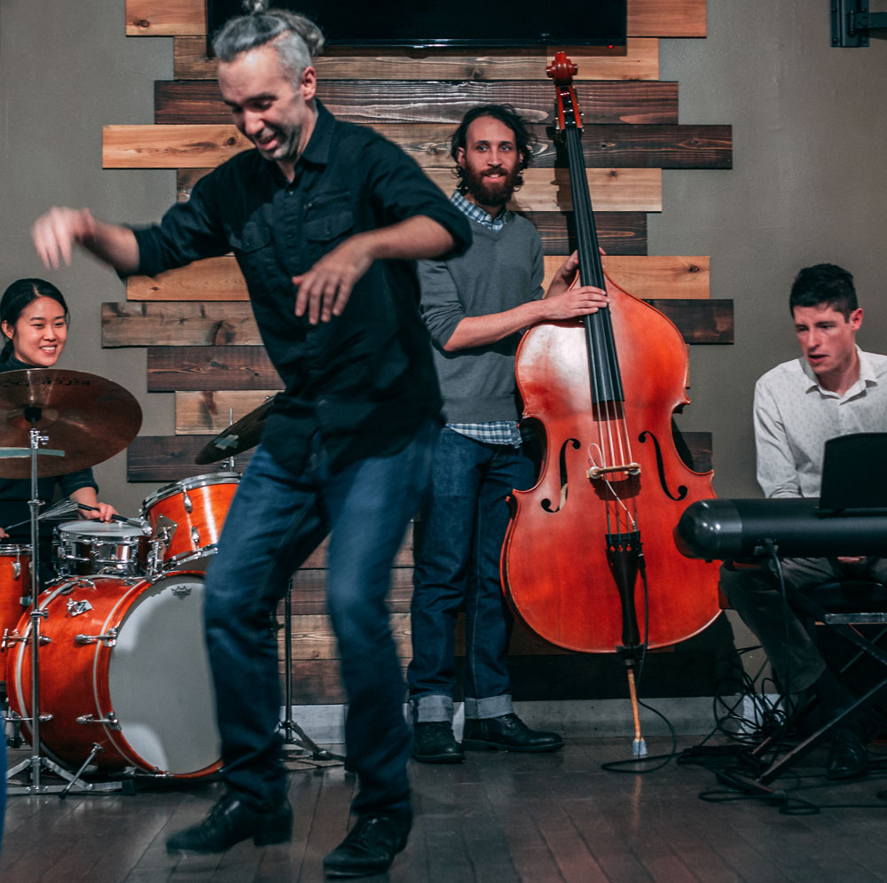 Andrew Nemr taps in front of a three piece band