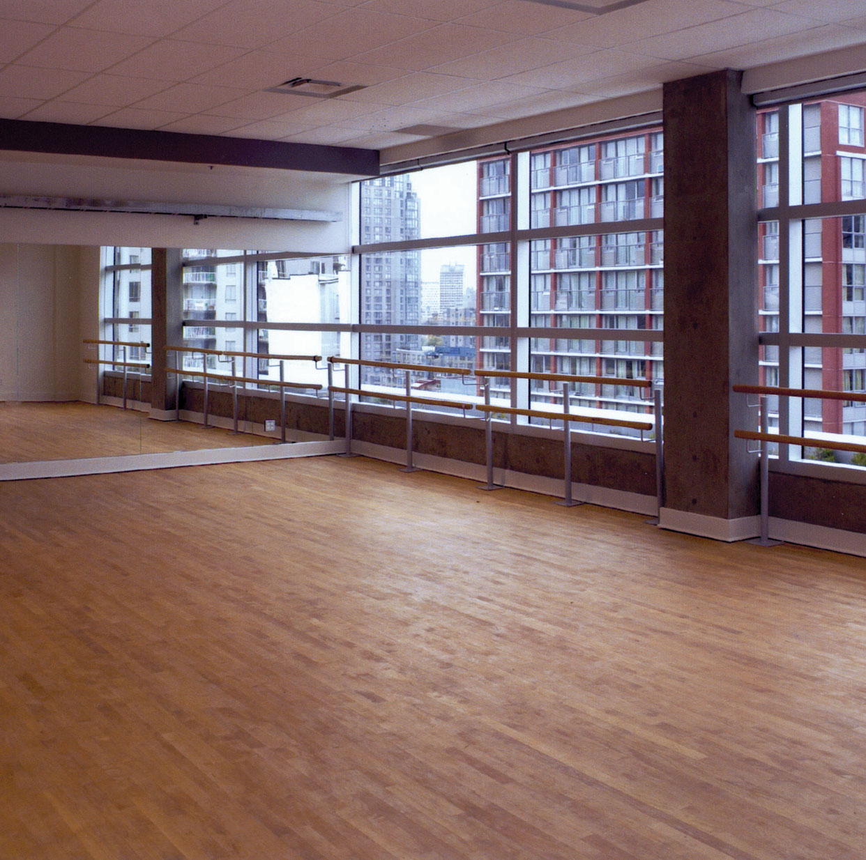 A bright empty dance studio. There is a long mirror on one wall and barres across a wall of windows.