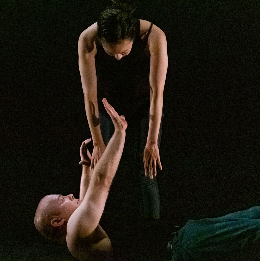 A dancer from All Bodies Dance Project leans down over top of another dancer, reaching up