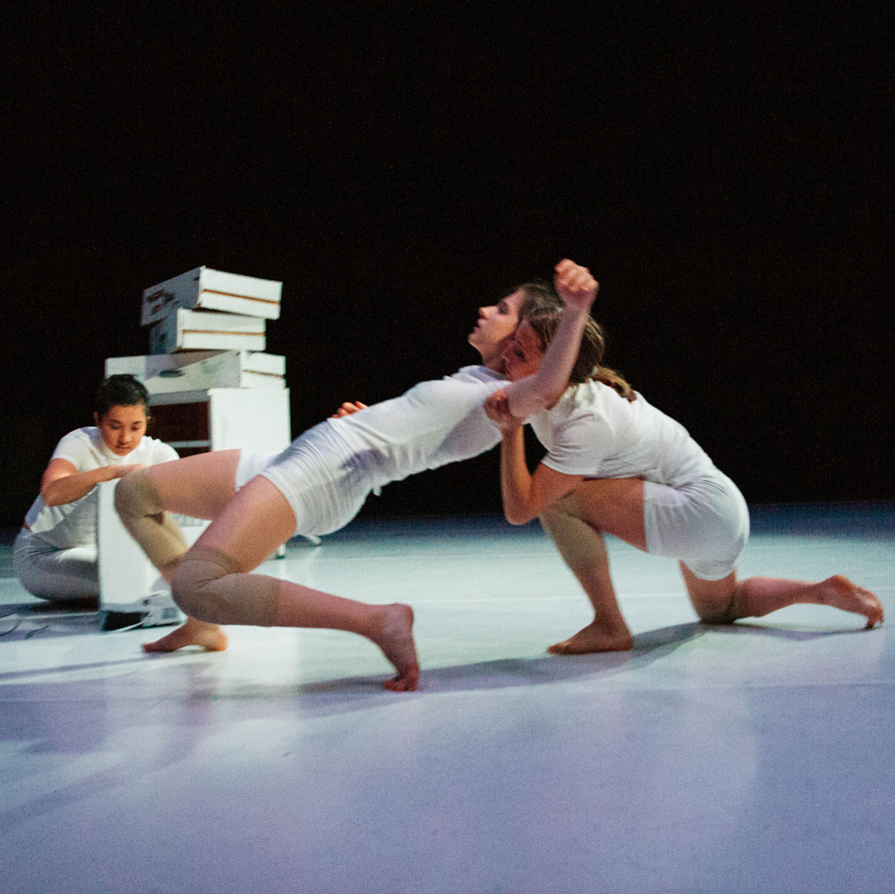 Two dancers from Clala Dance Project perform while another leans behind them