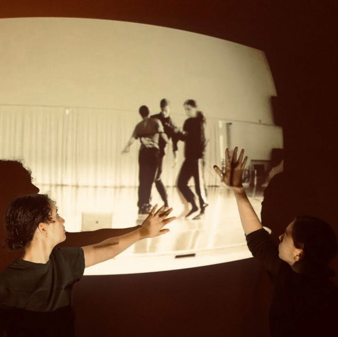 Madeleine Gilbert and Miakanese Manning pose in front of a project of dance artists performing.