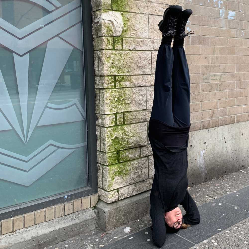 Dance artist P. Megan Andrews stands on her head outside a building