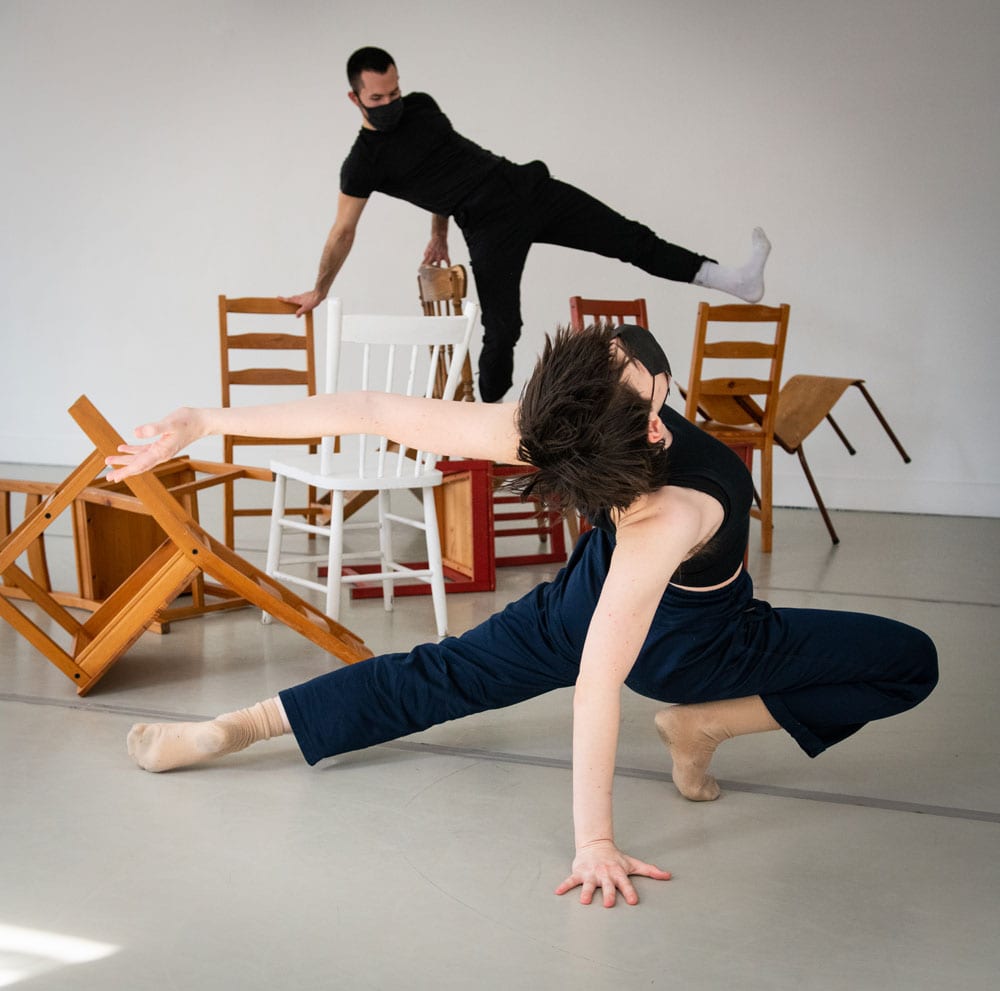 Dance artists perform over chairs and other furniture