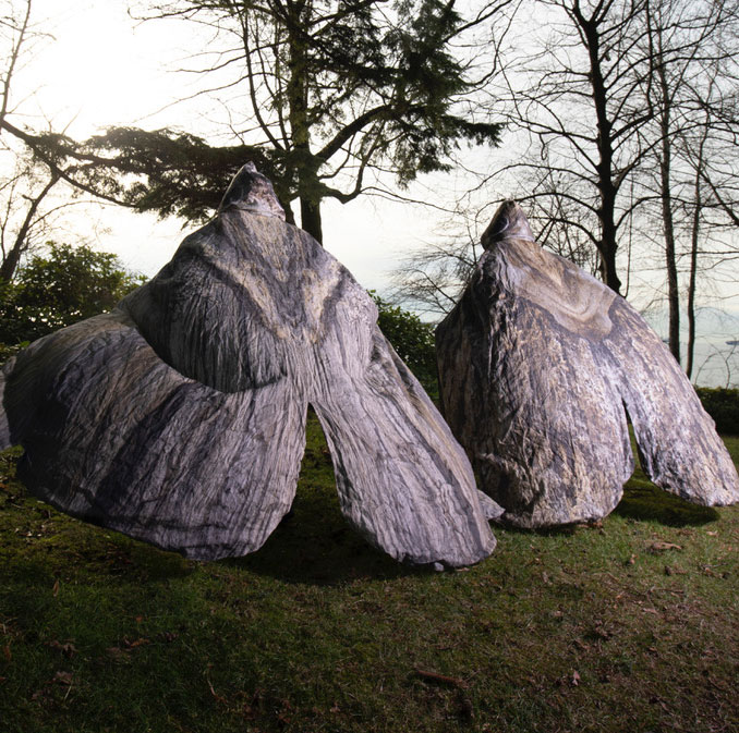 Two dance artists stand in a field wearing large moth costumes covering their entire backs