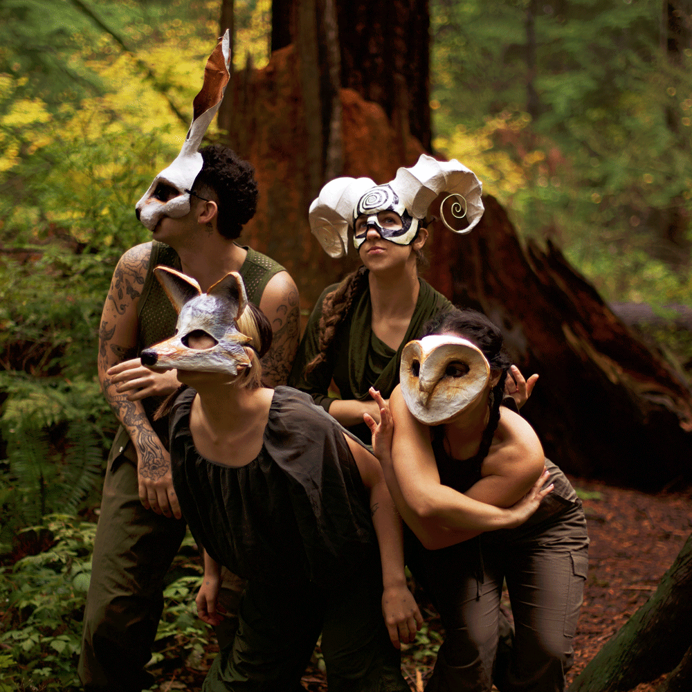 Four dance artists pose in the forest. They are wearing all green and white animal masks.